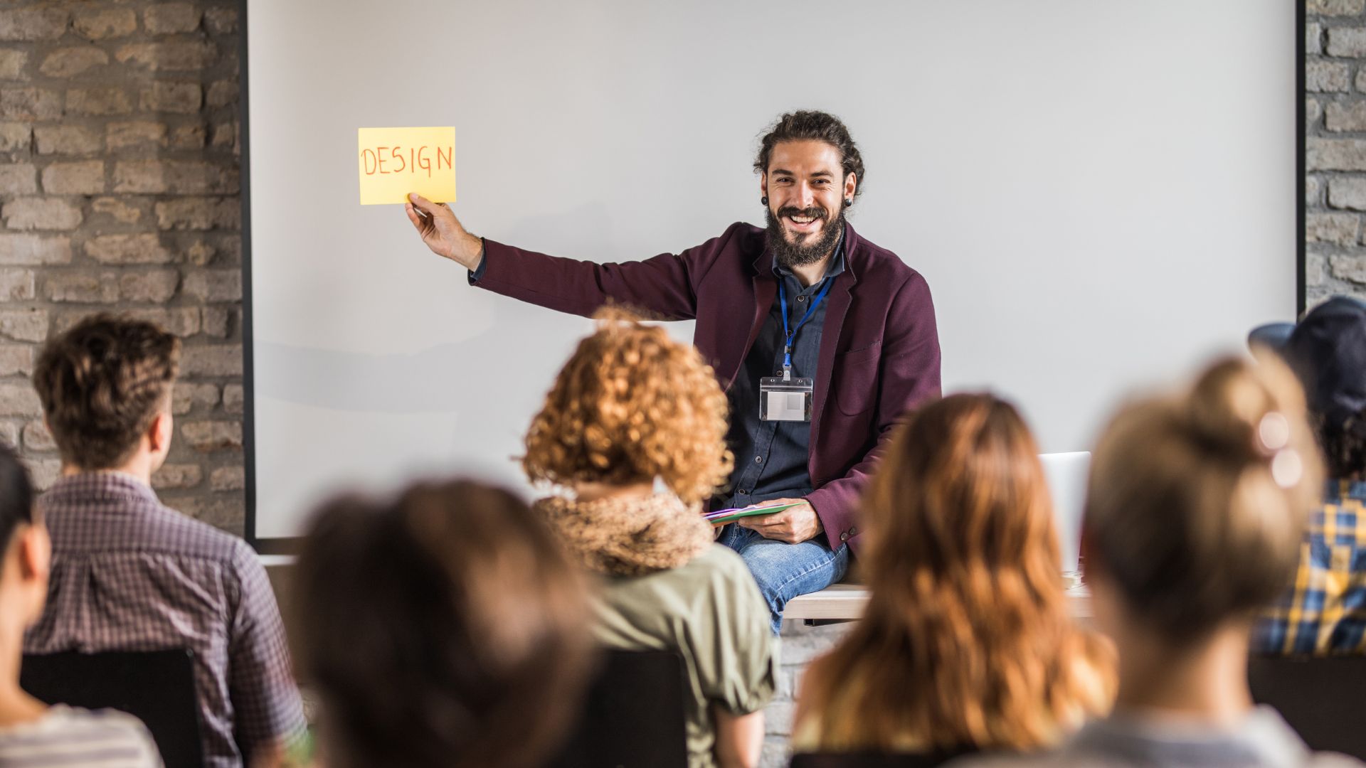 Profesor sonriendo mientras enseña un taller de diseño, representando la creatividad en la educación en un aula universitaria.