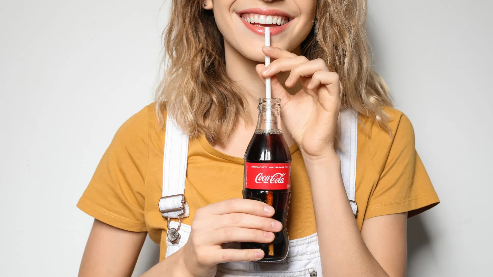 Mujer sonriendo mientras bebe una Coca-Cola, ejemplo visual de cómo las marcas generan conexión emocional — qué es branding.