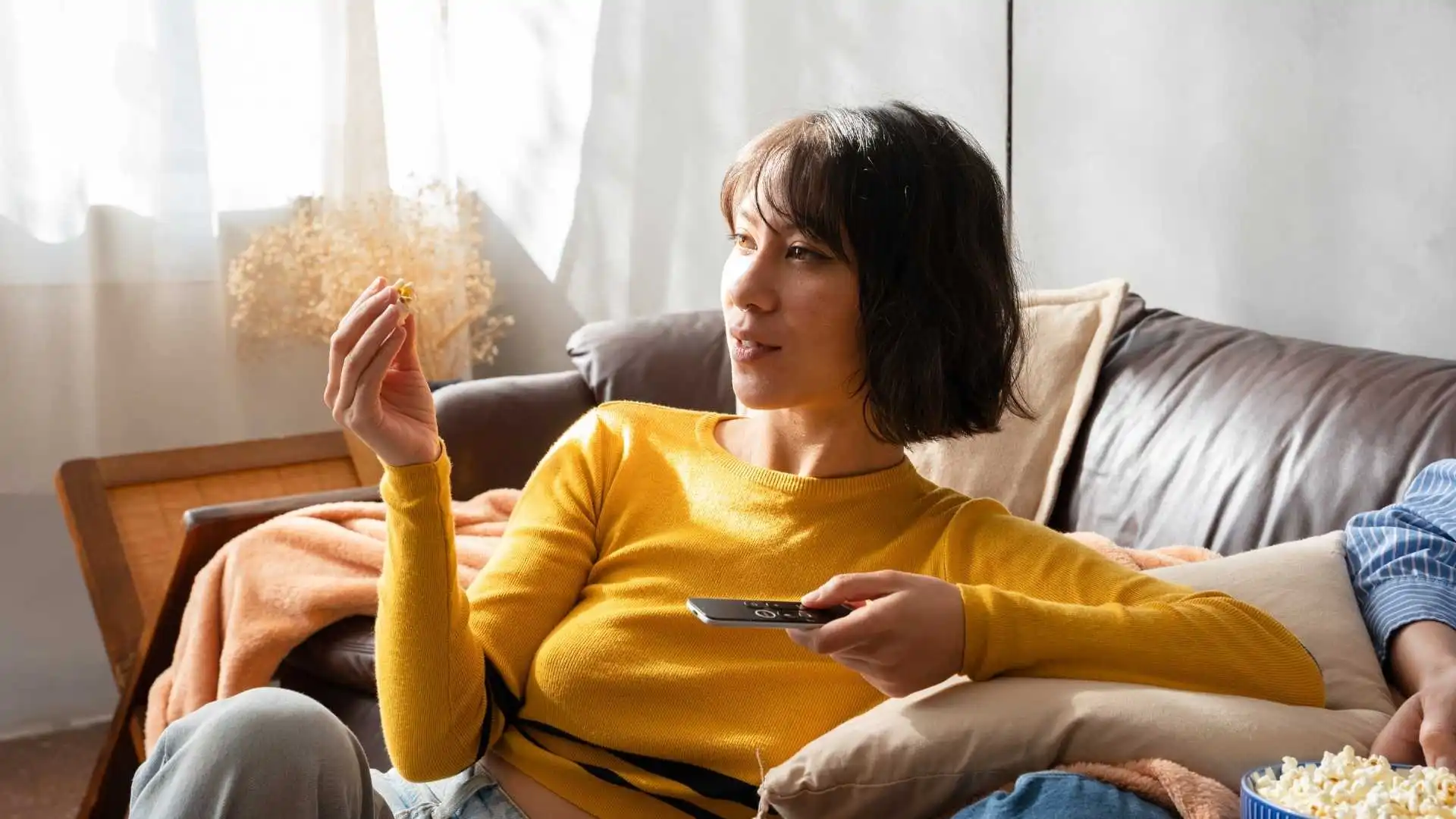 Mujer sentada en un sillón viendo televisión y comiendo palomitas, ideal para ilustrar recomendaciones de películas de drama en Prime Video.