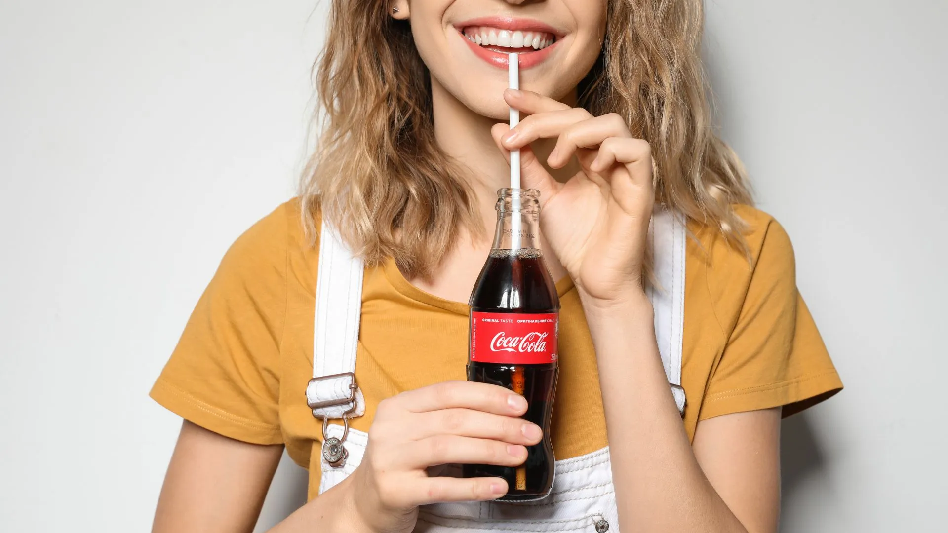 mujer sonriendo mientras bebe Coca-Cola de botella de vidrio con popote, muy al estilo de los mejores anuncios de coca cola