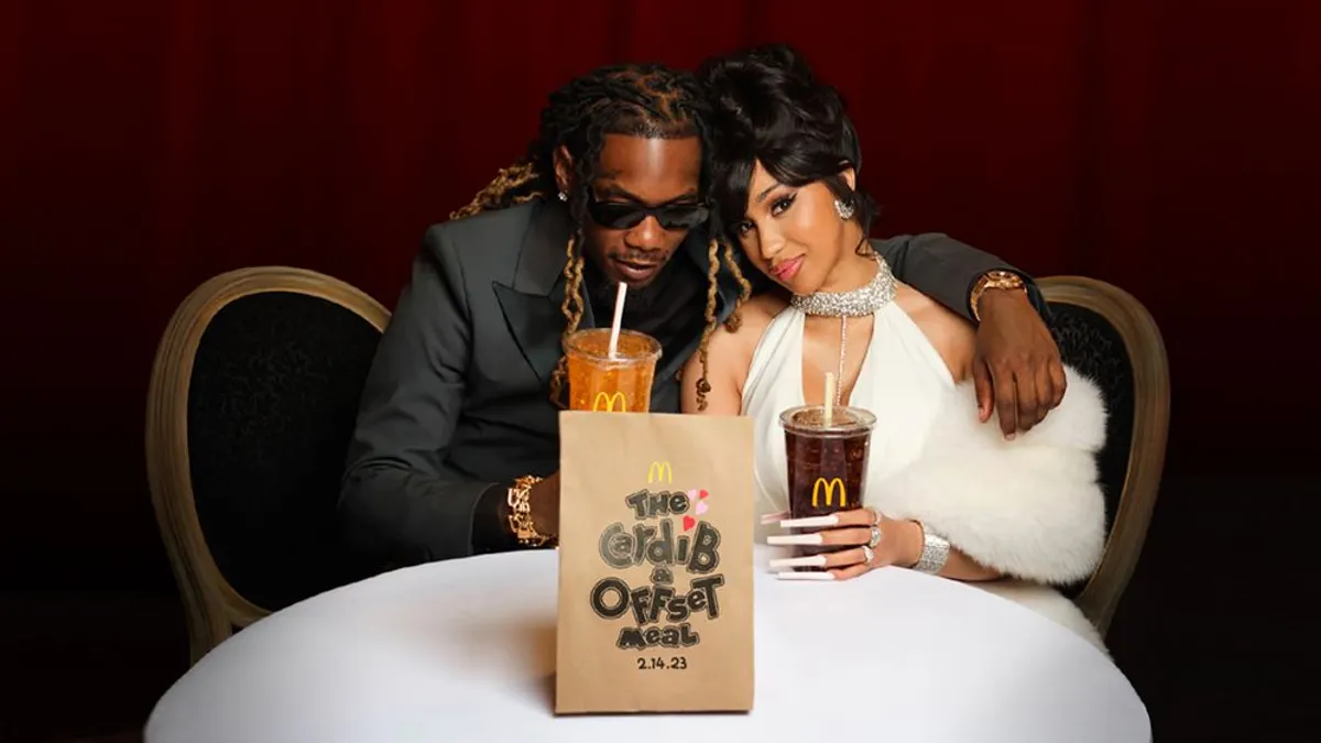Cardi B y Offset posan juntos en una mesa con bebidas y una bolsa de McDonald’s promocionando The Cardi B & Offset Meal.
