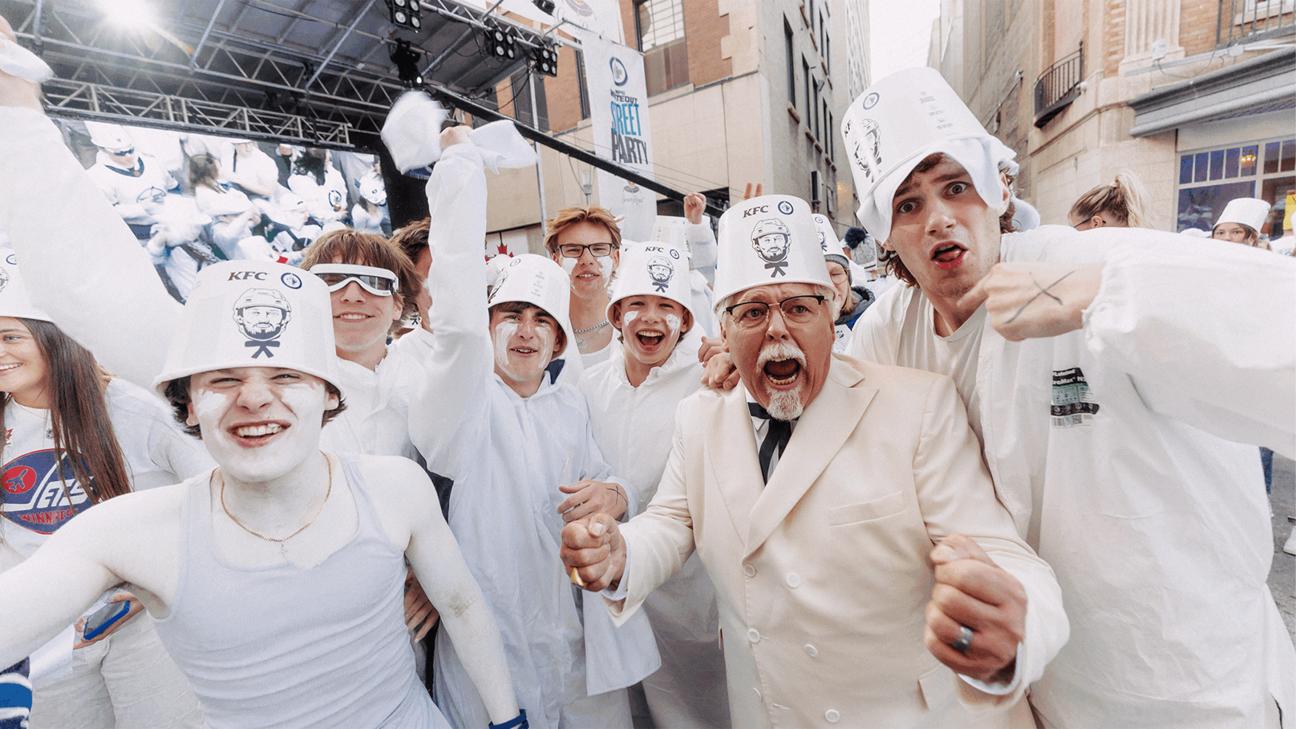 Grupo de fans de KFC vestidos de blanco junto al Coronel Sanders durante una activación promocional en la calle.