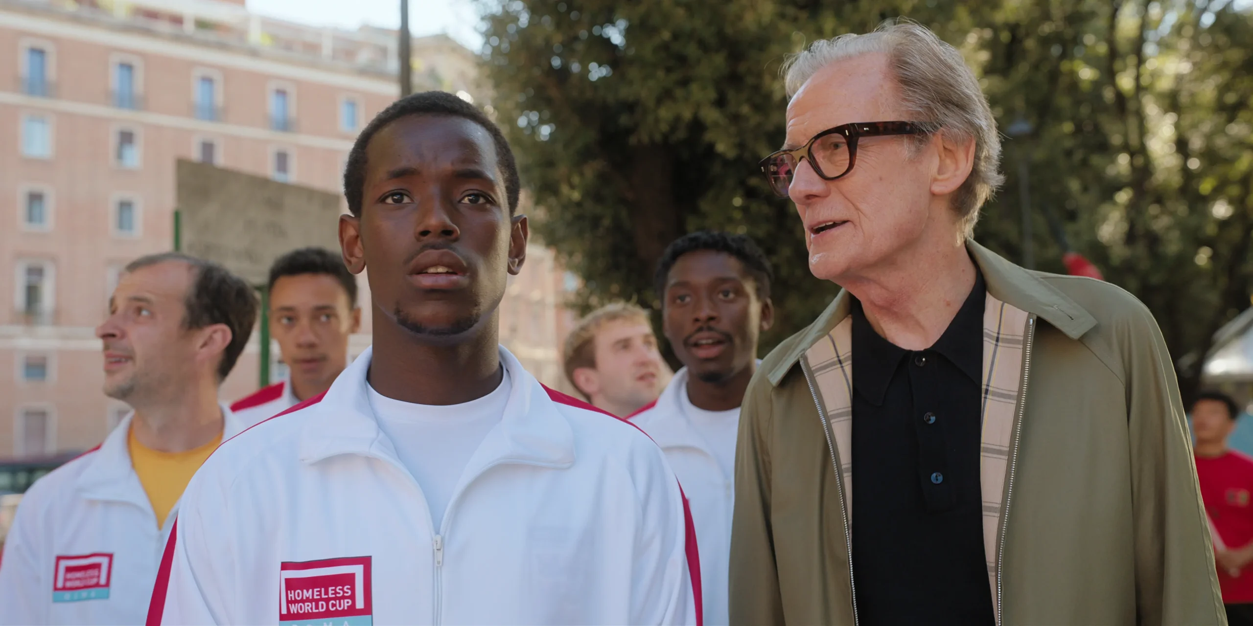 Escena de The Beautiful Game (2024), una de las películas de futbol más recientes, con jugadores de la Homeless World Cup acompañados por su entrenador.