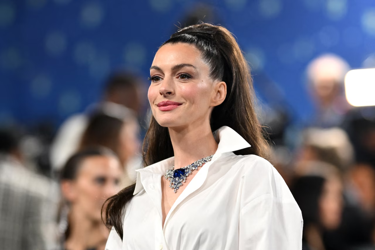 Anne Hathaway en un evento público, con camisa blanca y el cabello recogido.