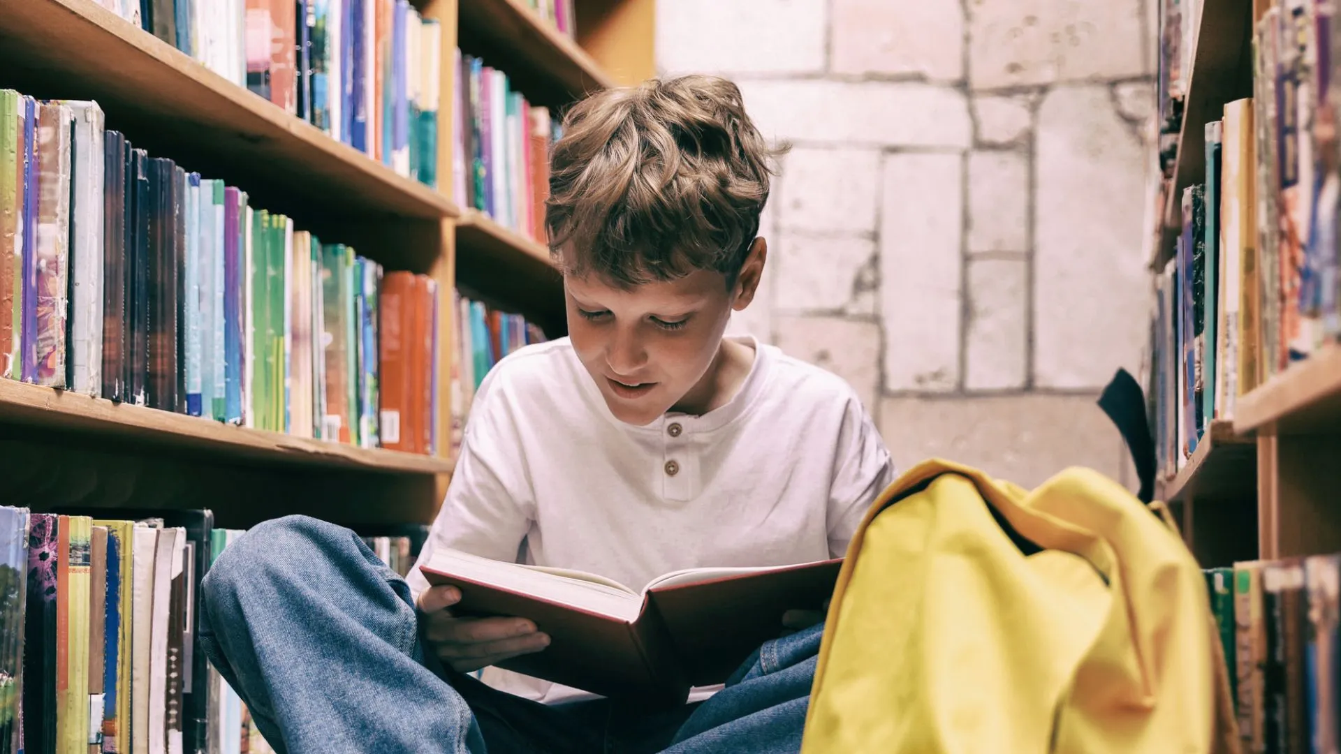 Adolescente leyendo un libro entre estanterías de una biblioteca